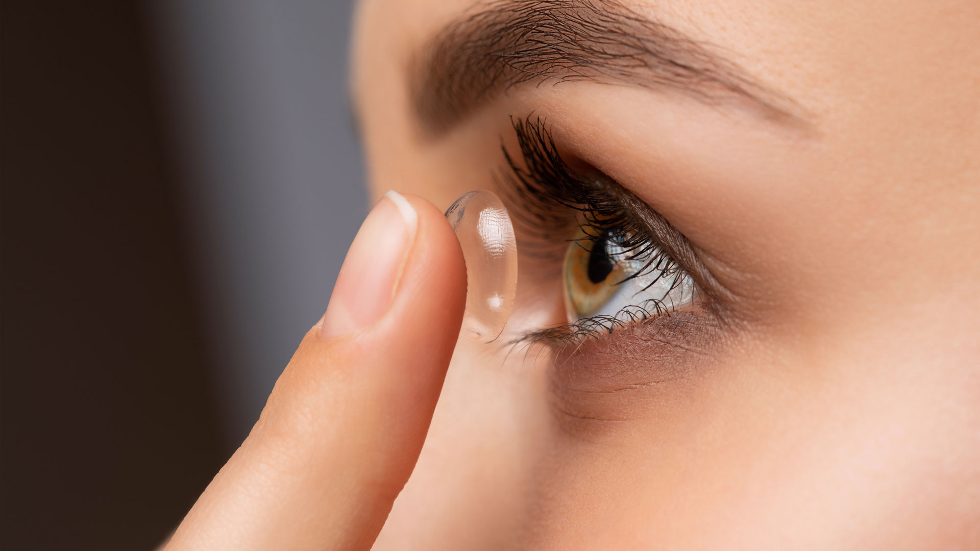 Beautiful woman holds contact lens on her finger. Eye care and the choice between the means to improve vision.