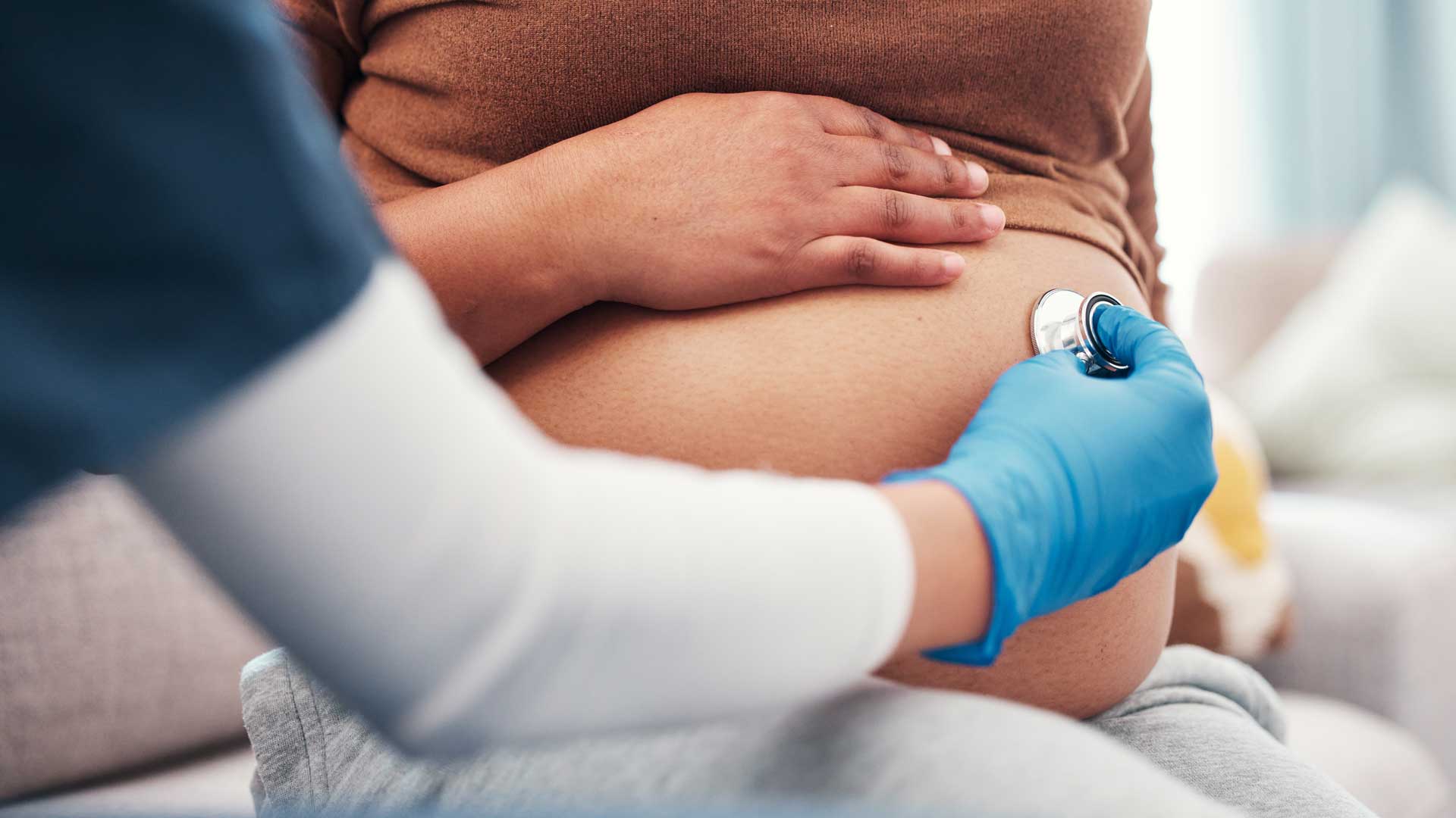 Closeup, pregnant and woman with healthcare checkup and stomach with wellness, appointment and results. Zoom, pregnancy and female with doctor, stethoscope and medical professional for consultation, m360 Research, hyperemesis gravidarum